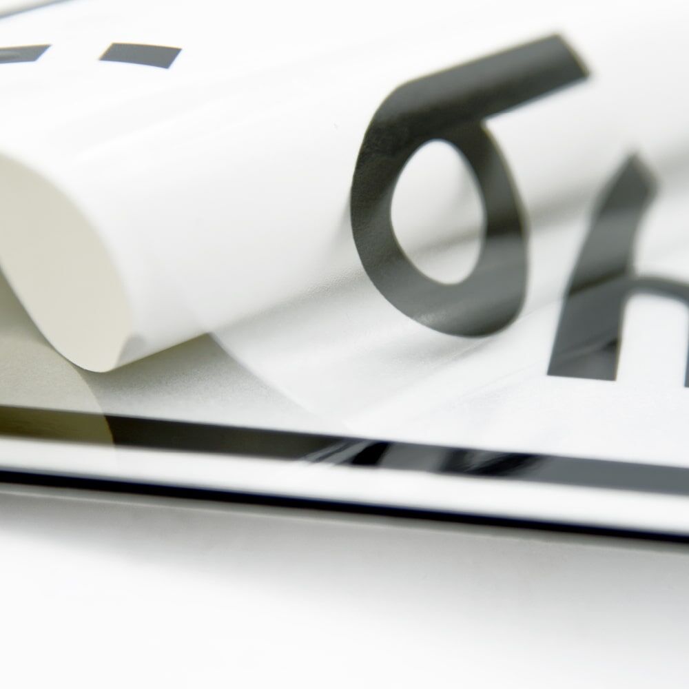 Transparente Overlay-Folie mit schwarzem Schriftzug, aufgelegt auf Zusatzschild, Randansicht