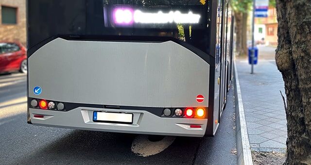 Die Rückseite eines weißen Busses mit Rücklichtern und einem Einbahnstraßen-Verbotsschild auf der Straße.