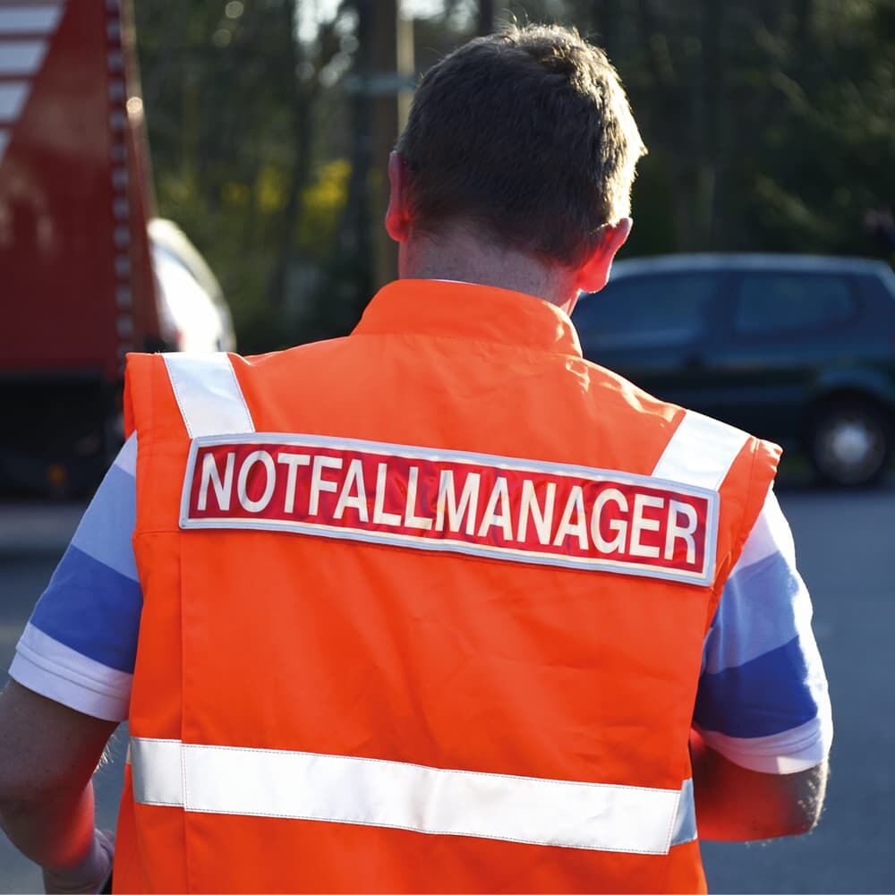 Orange Warnweste mit silbernem 3M Scotchlite 8925 Reflexband und Aufschrift „NOTFALLMANAGER“