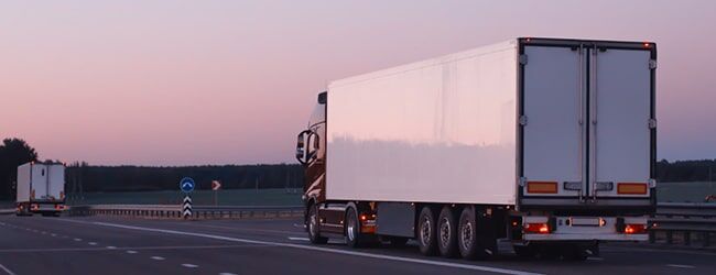 Weißer LKW mit Anhänger auf leerer Autobahn bei Dämmerung mit violettem Himmel.