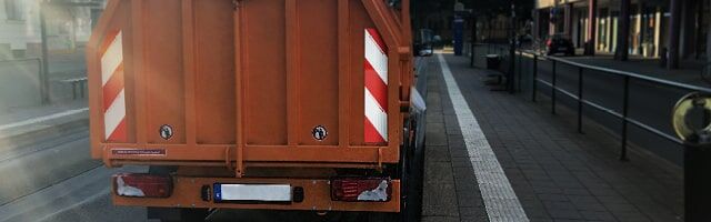 Sonderrechte gemäß § 35 StVO Rückansicht eines orangefarbenen Müllwagens am Straßenrand mit Warnstreifen