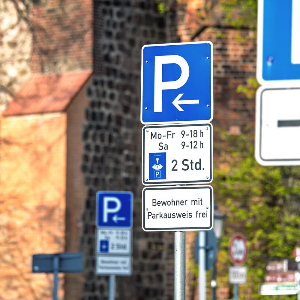 Parkschild „P“ mit Pfeil nach links auf Mast im Straßenraum