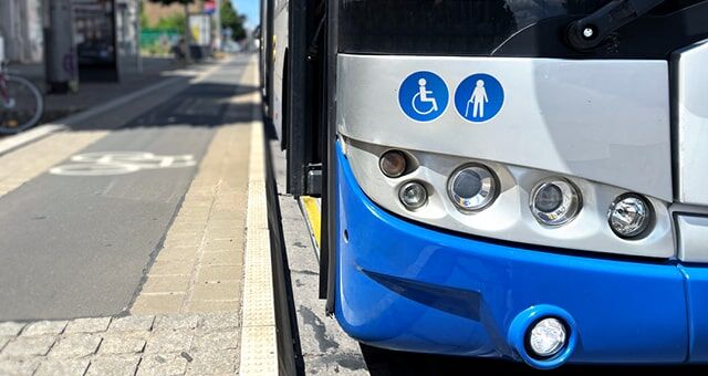 Vorderseite eines blauen Busses mit Hinweisschildern für Rollstuhlfahrer und Gehbehinderte an einer Haltestelle.