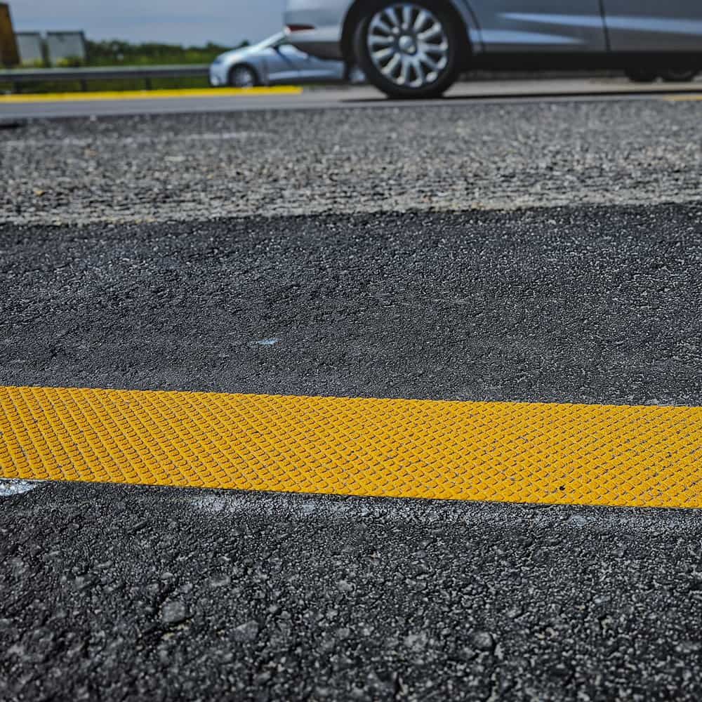 Gelbe Fahrbahnmarkierung aus 3M Stamark A721 auf dunklem Asphalt in Nahaufnahme