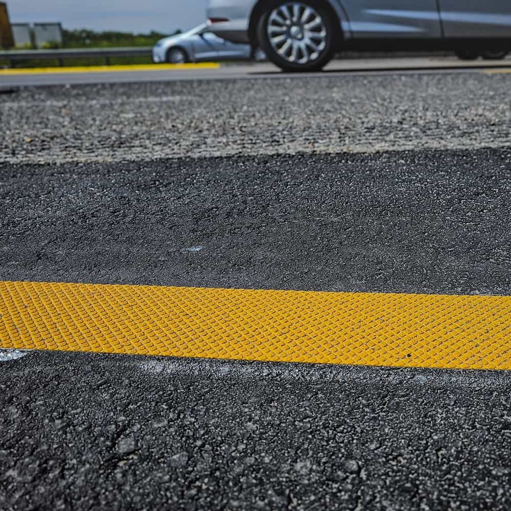 Gelbe Fahrbahnmarkierung aus 3M Stamark A721 auf dunklem Asphalt in Nahaufnahme