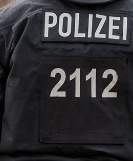 Ein Ausschnitt einer schwarzen Polizeiuniform mit reflektierendem „POLIZEI“-Schriftzug und der Nummer 2112.