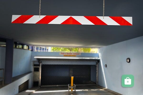Eine rot-weiße Industriewarnmarkierung auf Aluträger hängt als Höhenbegrenzung vor Tiefgarageneinfahrt.