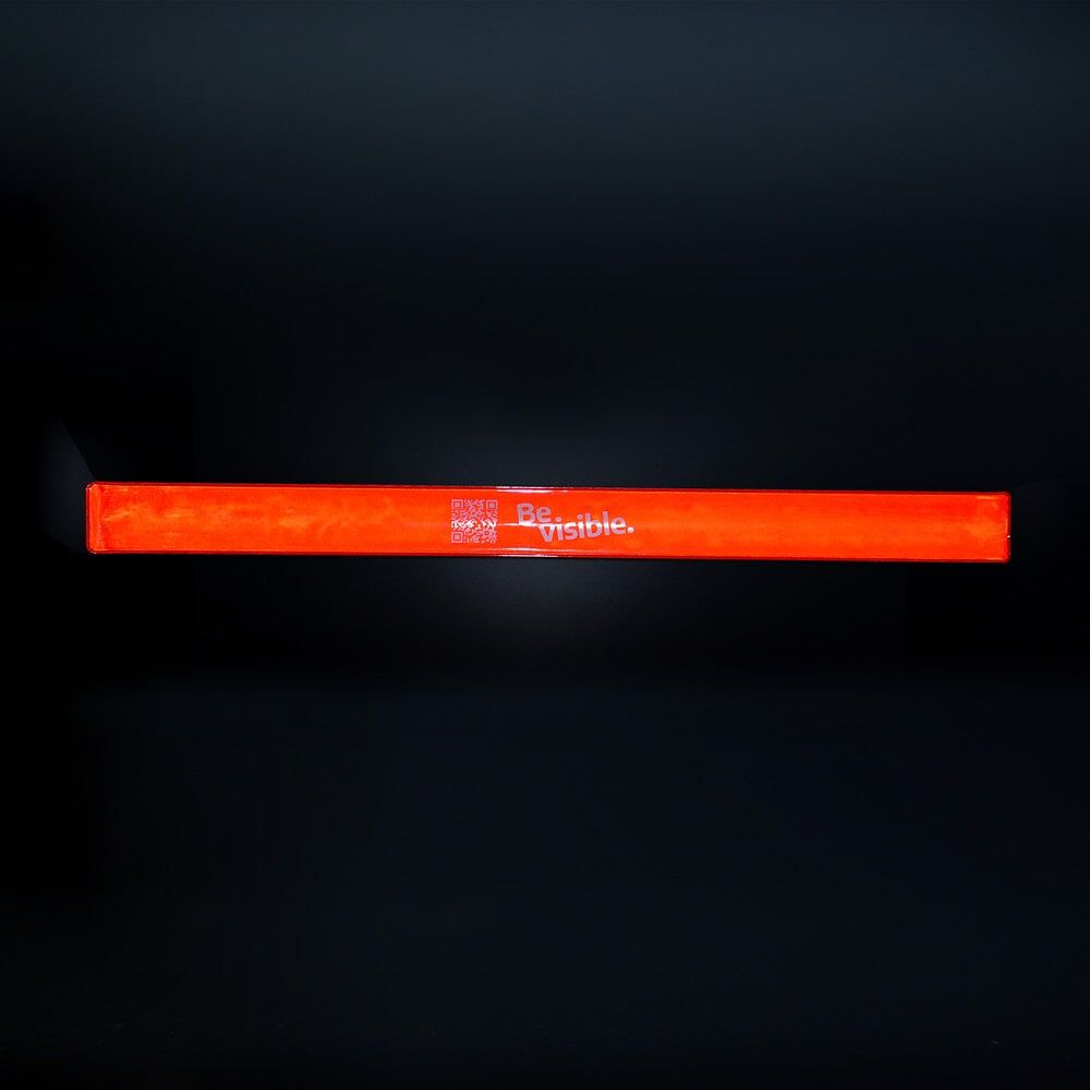 Schnapparmband rot reflektierend mit Schriftzug „Be visible.“ vor dunklem Hintergrund