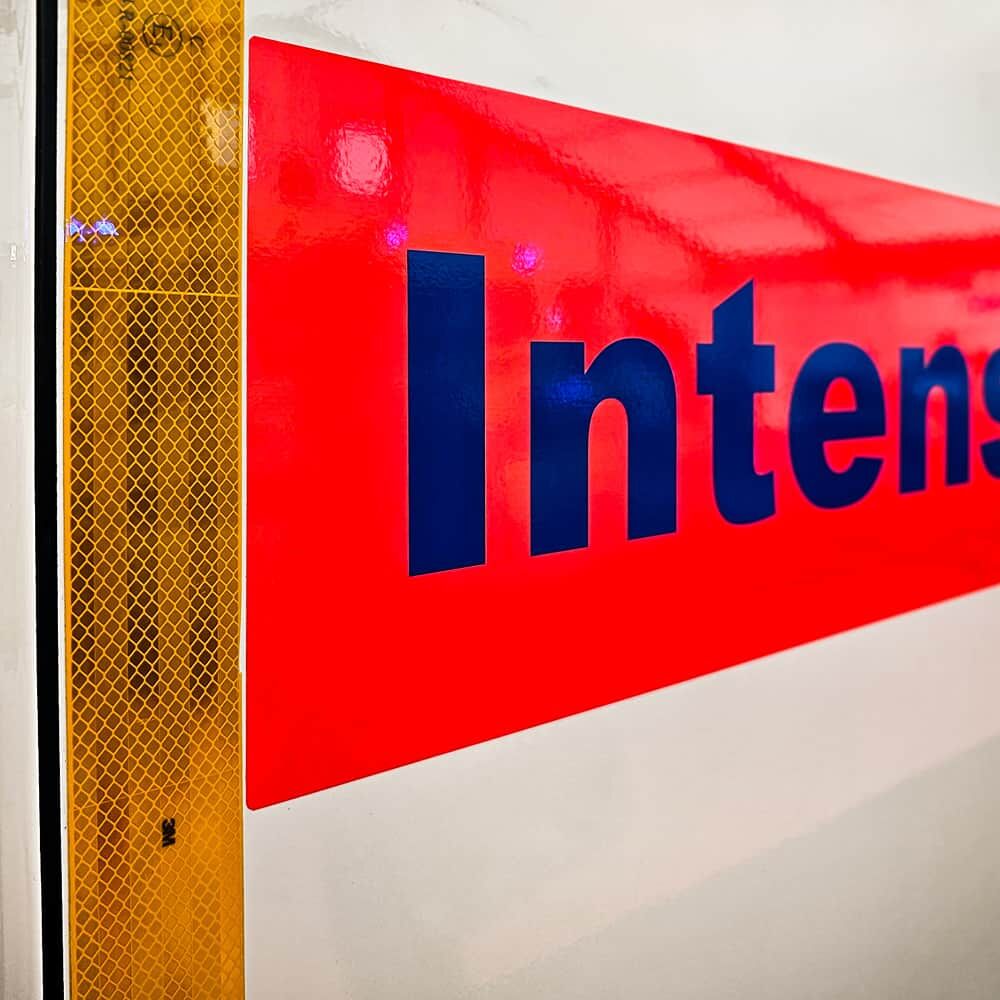 Fahrzeugseite mit vertikalem 3M 983 Konturstreifen fluor-gelb neben rotem Logo