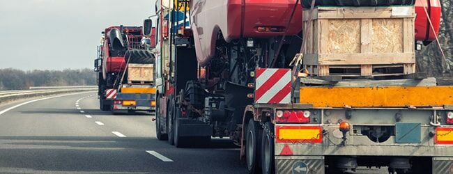 LKW-Autotransporter mit Fahrzeugen und Holzkiste auf der Ladefläche auf Autobahn unterwegs.