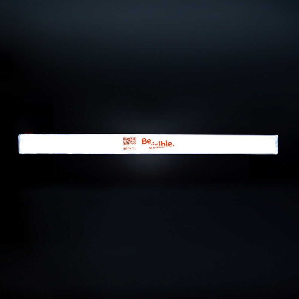 Schnapparmband weiß reflektierend mit Schriftzug „Be visible.“ vor dunklem Hintergrund