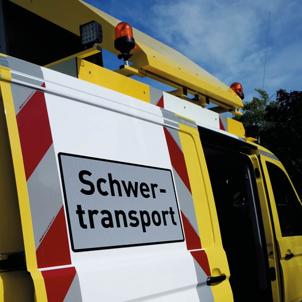 Schwertransportschild auf gelbem Begleitfahrzeug mit rot-weißer Warnmarkierung