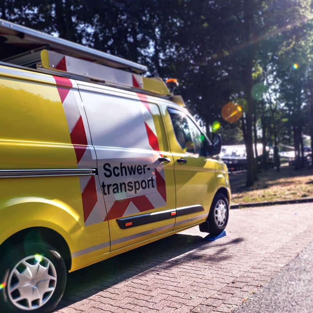 Gelbes Begleitfahrzeug, seitlich, rot-weiße ORALITE 5821 BF3 Warnmarkierung „Schwertransport“.