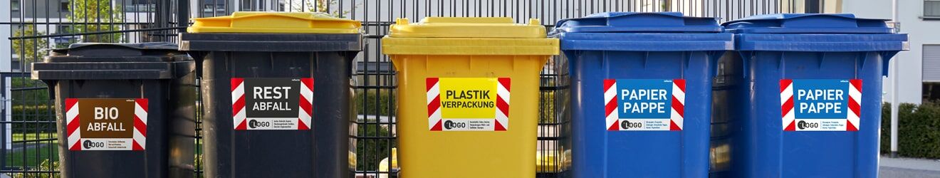 Sicherheitsaufkleber für Mülltonnen Das Bild zeigt verschiedenfarbige Mülltonnen mit Beschriftungen für Bioabfall, Restabfall, Plastik und Papier vor einem Zaun.