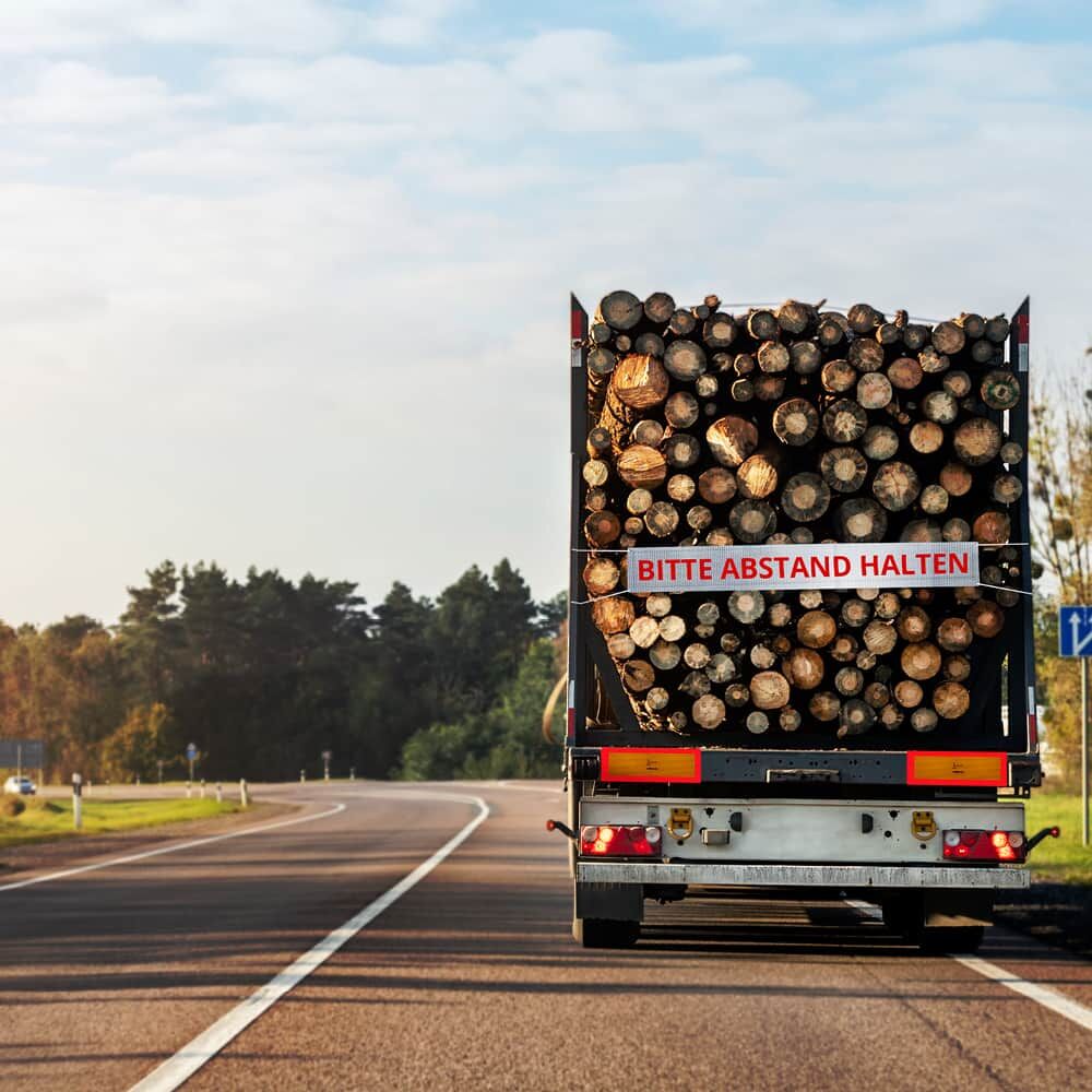 Hinweisbanner 5938MFLEX „BITTE ABSTAND HALTEN“ am Holztransport-Lkw auf Landstraße