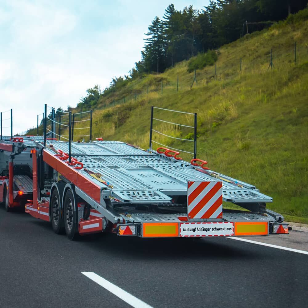 Montiertes „Achtung! Anhänger schwenkt aus“ Hinweisschild am Heck eines leeren Fahrzeugtransporters