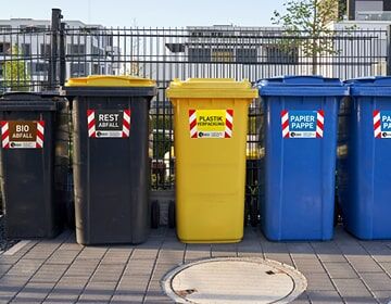 Sicherheitsaufkleber für Mülltonnen Bunte Mülltonnen in einer Reihe – schwarz, gelb und blau – für unterschiedliche Abfallarten.