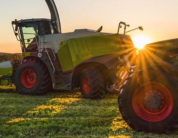 Das Bild zeigt einen großen Mähdrescher mit rot-weißen Warnmarkierungen auf einem Feld bei Sonnenuntergang.