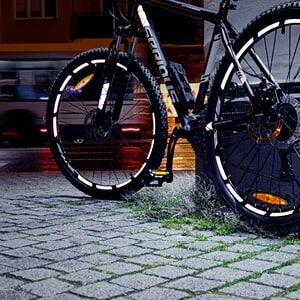 Mountainbike bei Nacht mit reflektierenden Felgenstreifen am Straßenrand.