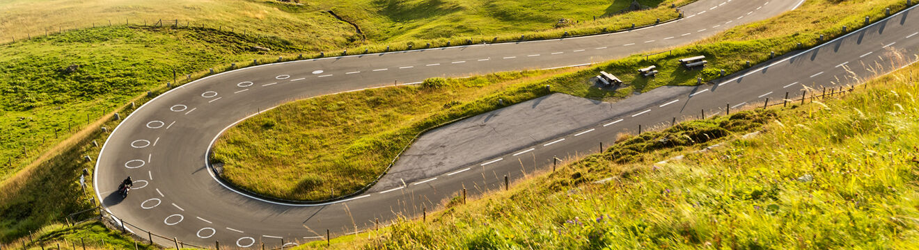 Weiße Ellipsen zur Kurvenmarkierung auf einer Serpentinenstraße mit Motorradfahrer