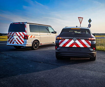 Zwei Fahrzeuge mit rot-weißer Warnmarkierung am Heck an ländlicher Kreuzung.