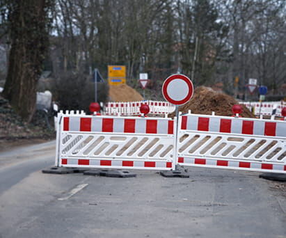 Straßensperrung mit rot-weißen Absperrelementen und Verbotsschild auf Baustelle.