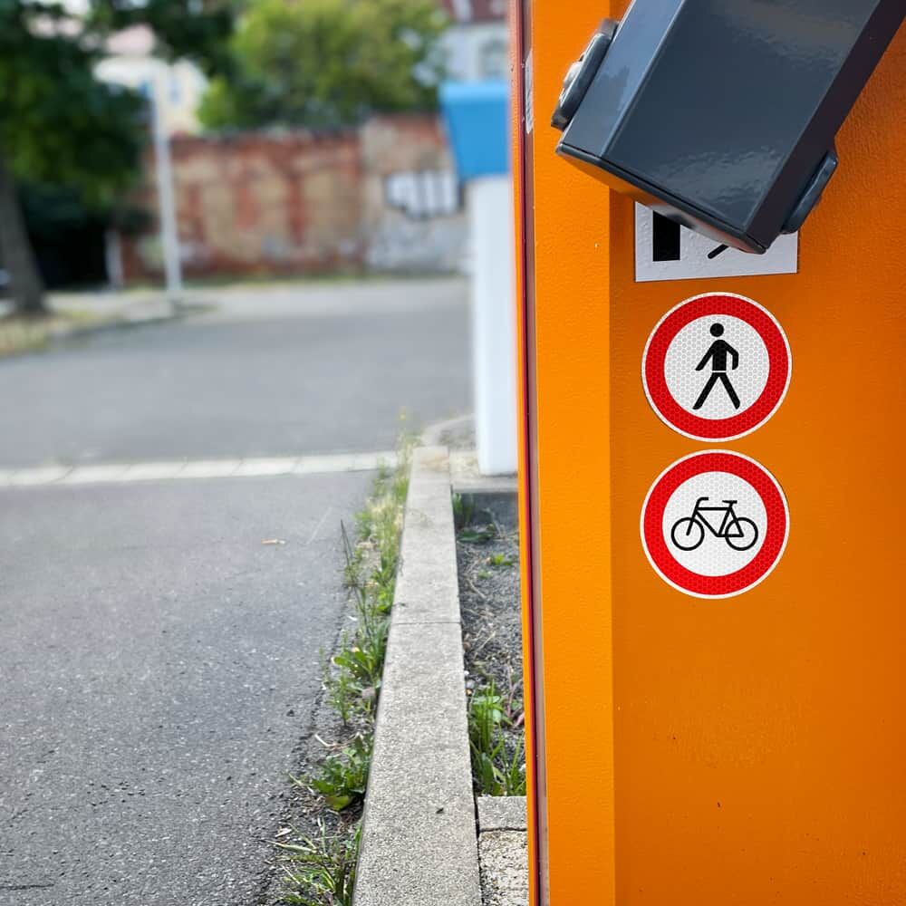 Radverkehr-verboten-Aufkleber an orangefarbener Schranke unter Fußgängerzeichen