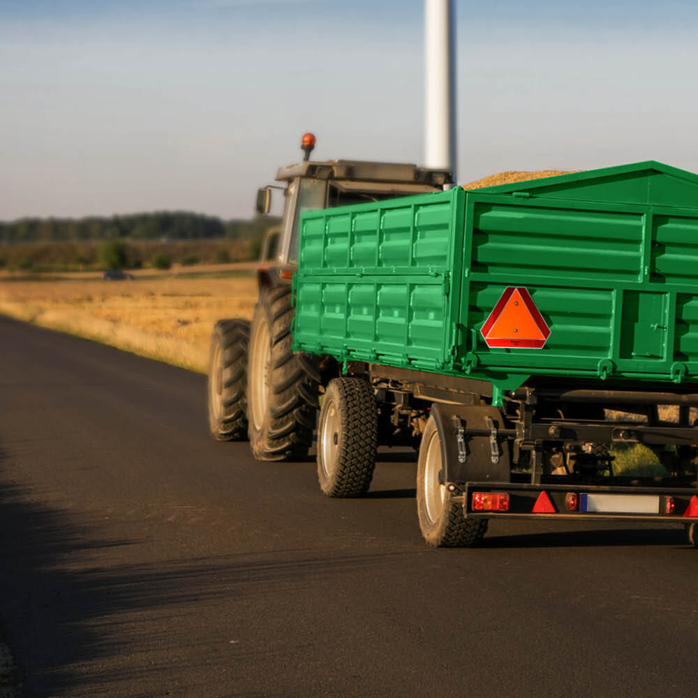 Warntafel am grünen Traktor-Anhänger auf Landstraße befestigt
