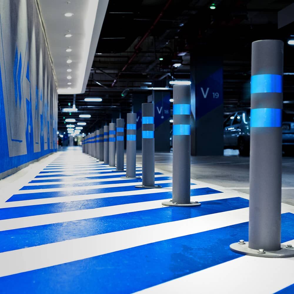 Graue Parkhaus-Poller mit blauem Reflexband 5600E markieren den Fußweg.