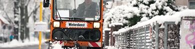 Winterdienstfahrzeug räumt Schnee von einem Gehweg in einer Wohngegend.