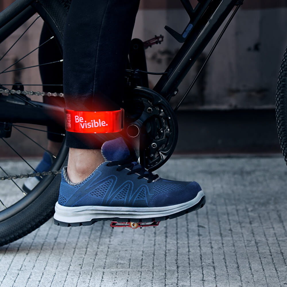 Radfahrerbein mit rotem reflektierendem Schnapparmband „Be visible.“ am Knöchel