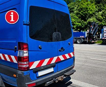 Blauer Transporter mit rot-weißen Warnmarkierungen, rotem i-Symbol und Anhängerkupplung von hinten.