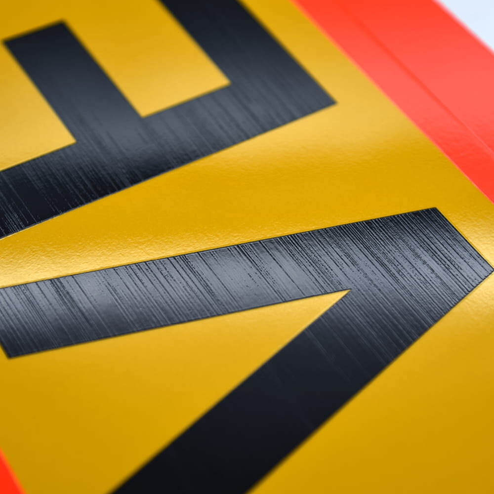 Nahaufnahme der reflektierenden Folienstruktur auf gelber Fläche mit schwarzer Schrift