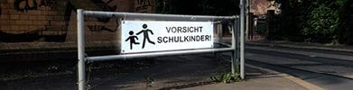 Warnschild mit Aufschrift „Vorsicht Schulkinder“ an einem Schulweg.