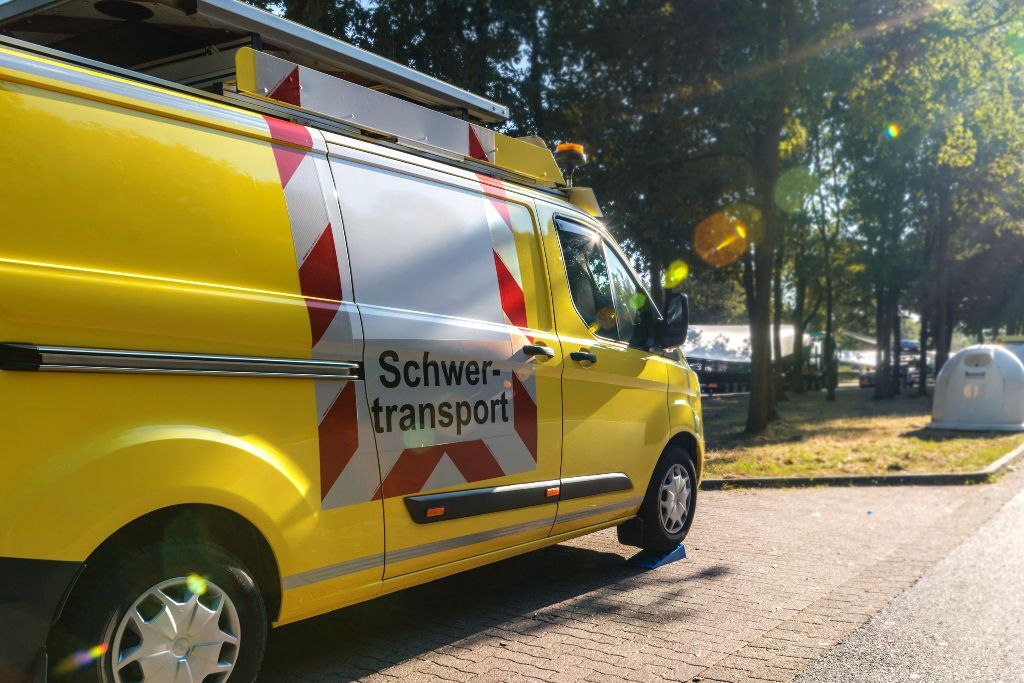 Gelbes Begleitfahrzeug mit Warnmarkieurng und "Schwertransport" Schild an der Seite