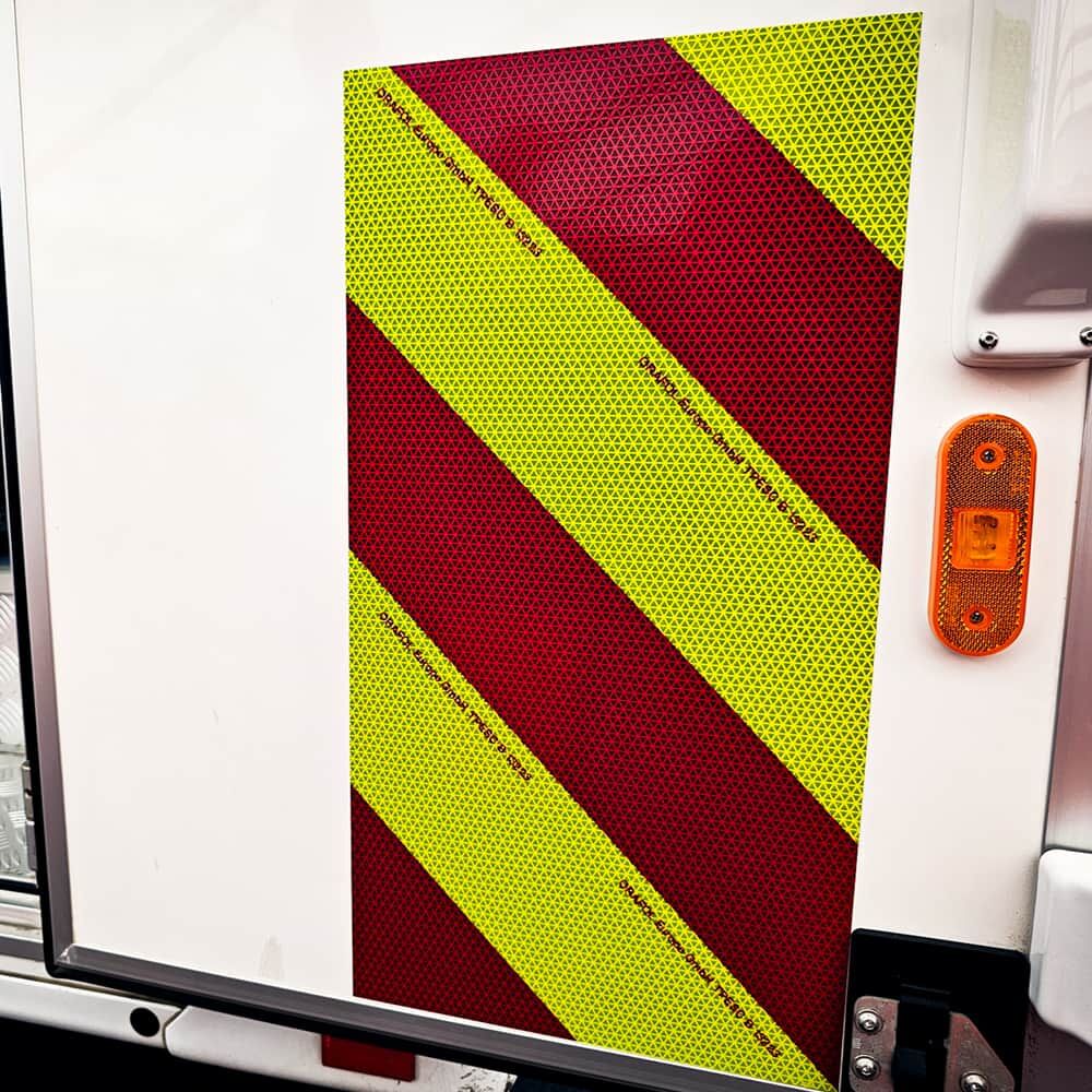 Gelb-rote ORALITE VC612 Folie diagonal auf weißer Fahrzeugseite montiert