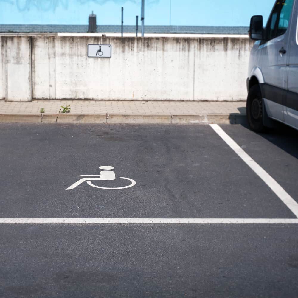 Parkplatz mit weißem Rollstuhlsymbol für Behindertenparkplatz, daneben Transporter