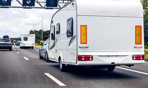 Abschnittstitelbild zu Heckwarntafeln Das Bild zeigt ein Wohnwagengespann aus Heckperspektive mit Hechwarnmarkierungen auf der Autobahn