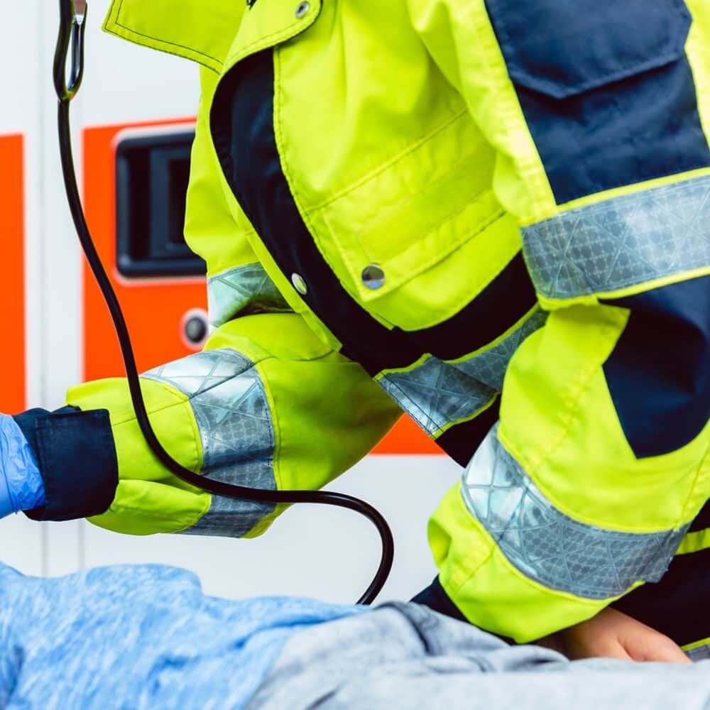 Rettungssanitäter in gelber Jacke mit silbernem GP340-Reflexband versorgt Patienten
