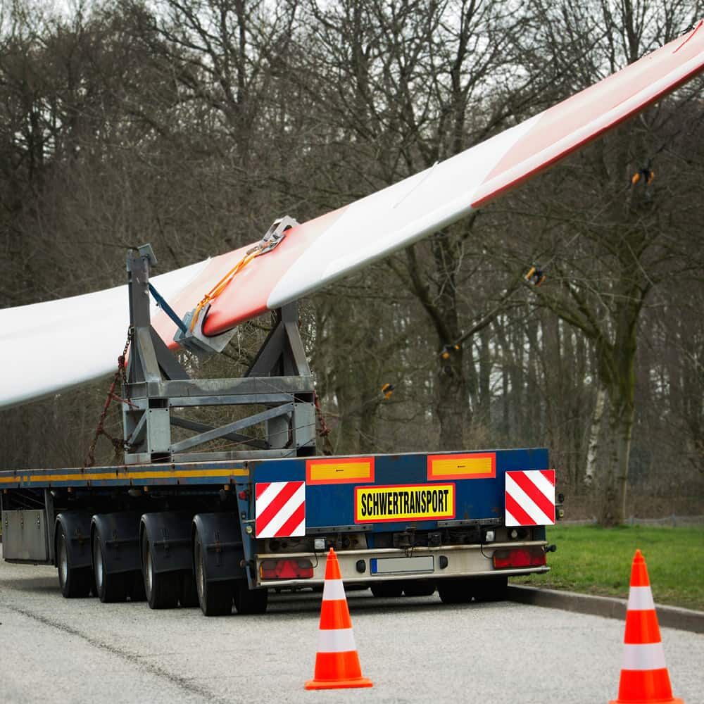 Schwertransporter mit Windradflügel und gelbem „SCHWERTRANSPORT“-Schild am Heck