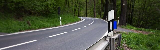 Wildwarnreflektoren Kurvenreiche Landstraße durch bewaldetes Gebiet mit Leitpfosten und aufmontiertem Wildwarner am Straßenrand