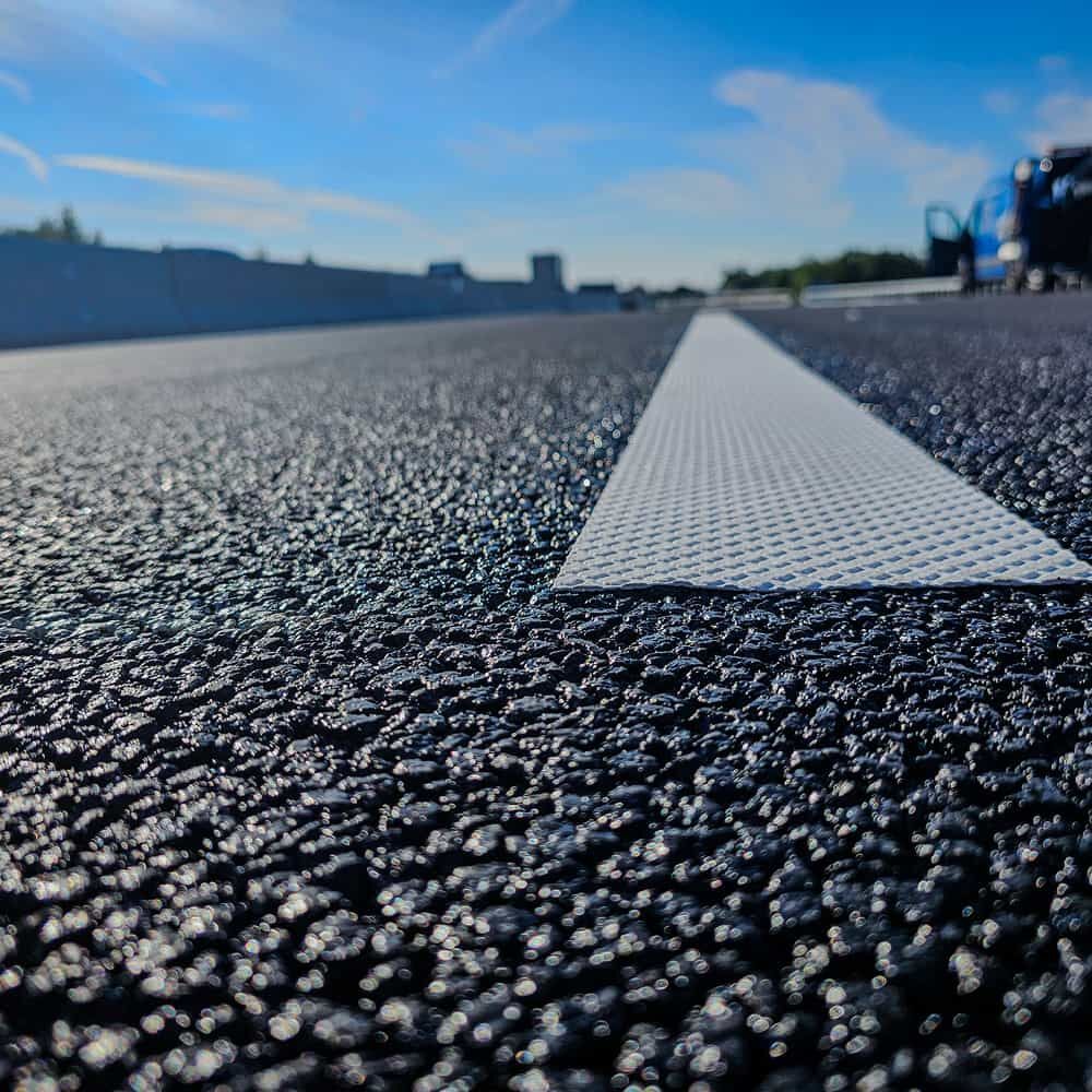 Weiße Markierungsfolie flach auf dunklem Asphalt in niedriger Perspektive