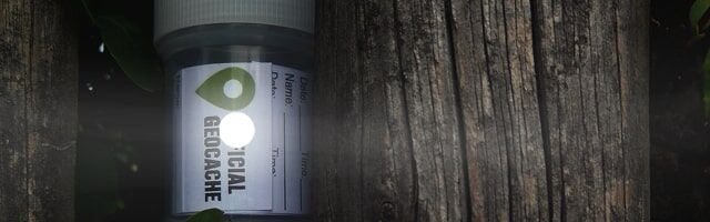 Ein Pillenbehälter mit Reflexsticker und einem Geocache-Etikett an einem dunklen Holzpfosten.