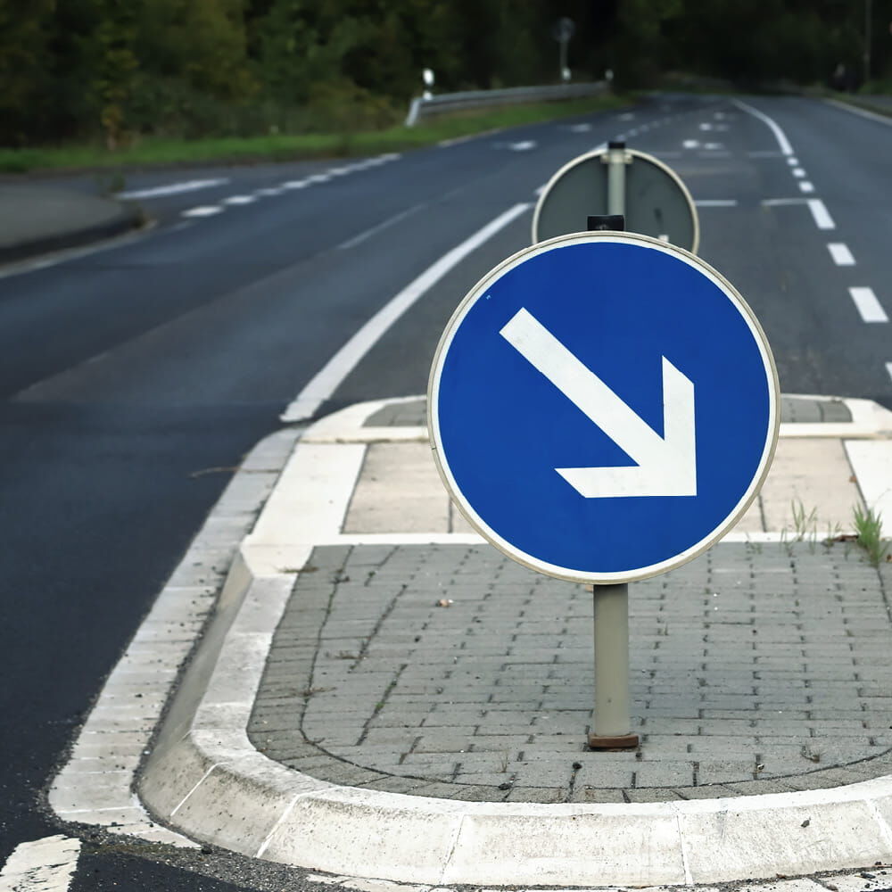 VZ 222 „Vorgeschriebene Vorbeifahrt links“ am Straßenleitpfosten auf Fußgängerinsel