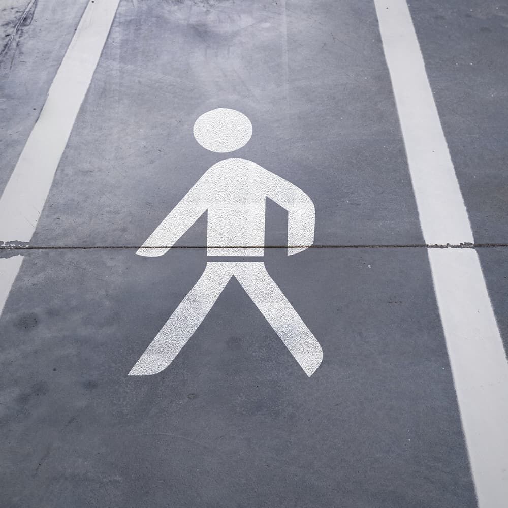 Verklebtes 3M Stamark Fußgänger-Symbol in Verkehrsweiß auf Asphaltoberfläche