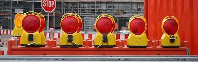 Reihe gelber Baustellenlampen mit roten Warnleuchten vor einem Stoppschild