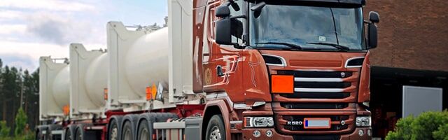 ADR Gefahrgutwarntafeln Ein roter Containerfahrzeug für Gefahrgut mit Gefahrgut-Warntafeln, beladen mit weißen Tankcontainern.