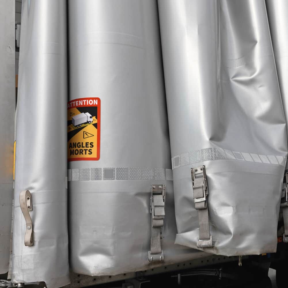 Warnschild „Angles Morts“ auf gefalteter Lkw-Plane welche mit silbernen Gurten befestigt ist