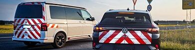 Zwei Fahrzeuge mit rot-weißer Warnmarkierung parken am Straßenrand.