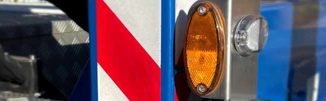 Rückstrahler – Reflexfolie statt Kunststoff-Rückstrahler Ein blauer Pfosten mit rot-weißer Warnmarkierung und einem orangefarbenen Reflektor.